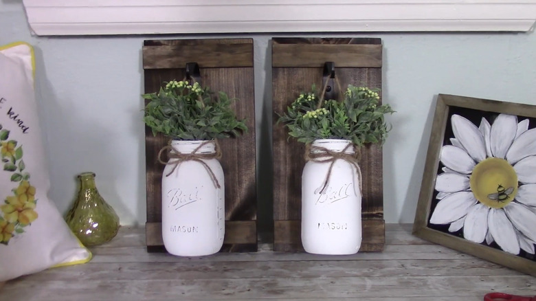 Two wall hangings with plank backgrounds and faux flowers in a Mason jar