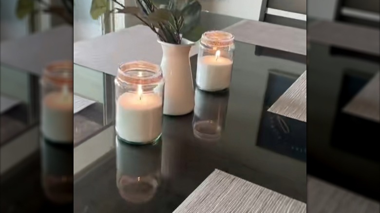 Two bead candles made in old pickle jars with lace around the top sitting on a table