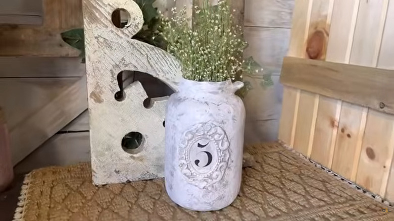 A large pickle jar decorated to look like pottery with dried flowers in it