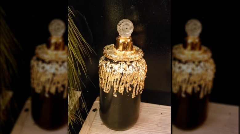 A pickle jar painted black with gold leaf accents and a glass topper
