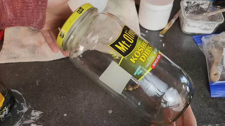 A pair of hands holding a pickle jar near a table with craft supplies
