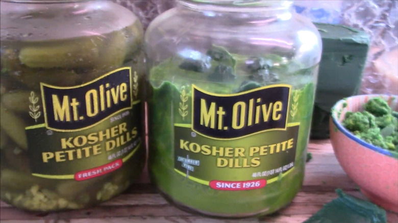 A jar of pickles next to a pickle jar with a candle that looks like pickles
