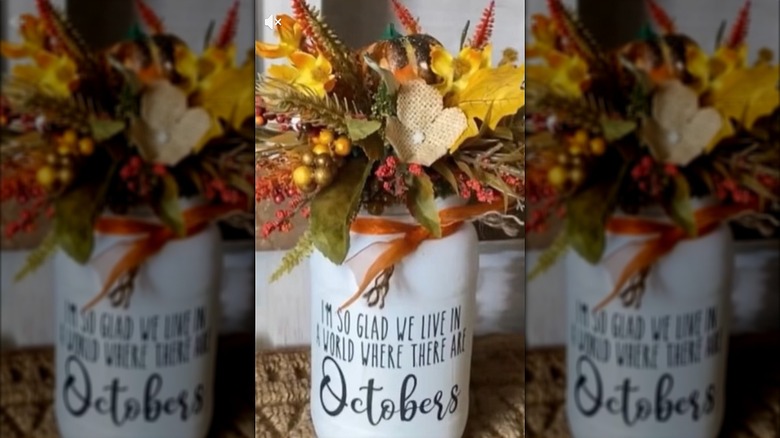 A pickle jar with faux fall florals attached to the top