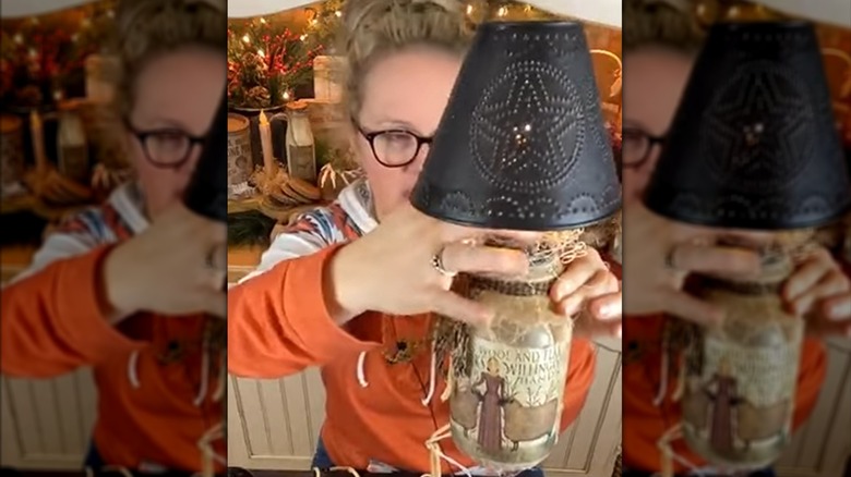 A person holding a lamp made from a pickle jar base and a punched tin shade