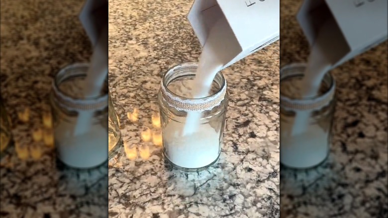 Woman filling repurposed pickle jar with lace trim with candle filler for DIY centerpiece on granite countertop