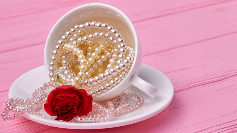 Pearl strands in teacup on saucer with rose