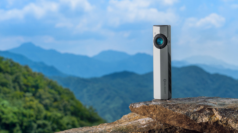 Olight ArkPro graphite flashlight on a rock in front of mountains