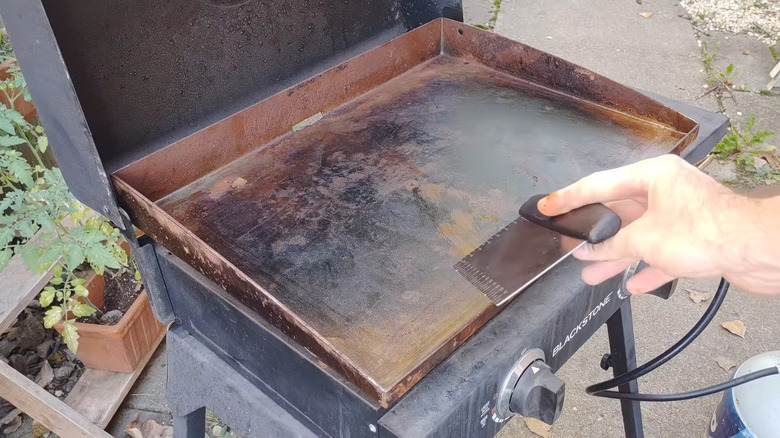 A rusty Blackstone griddle and a man preparing to clean it