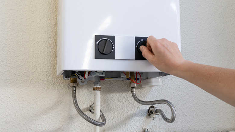 Person turning the dial on a tankless water heater.