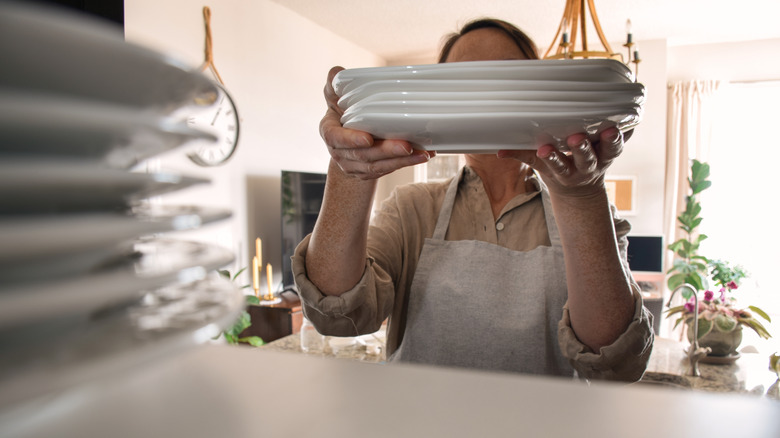 Woman placing a stack of plates inside a cabinet, seen from within the cabinet