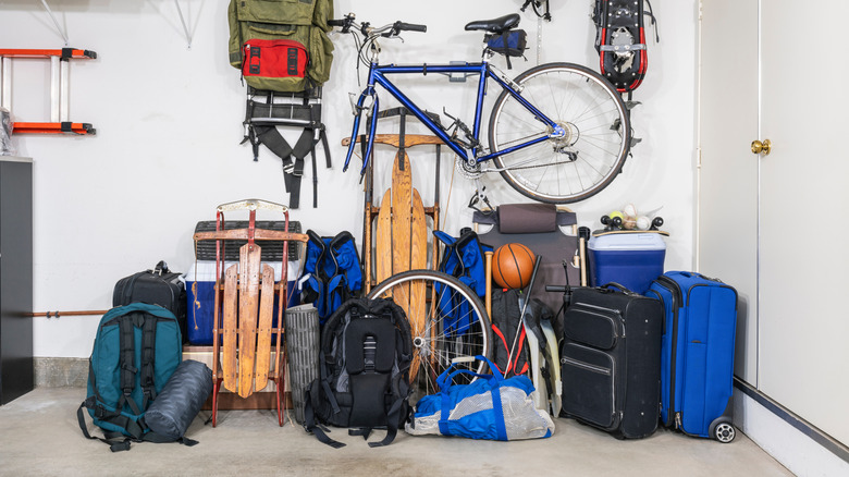 disorganized pile of sporting goods, travel stuff, and other miscellaneous items on the floor of a garage by the door to the house