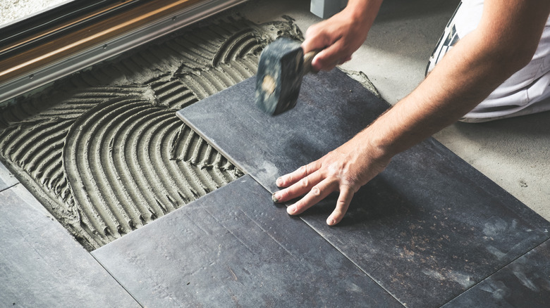 A worker uses a rubber mallet to lay black ceramic floor tiles