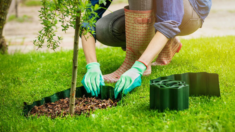A person wearing boots installs landscape edging around a tree