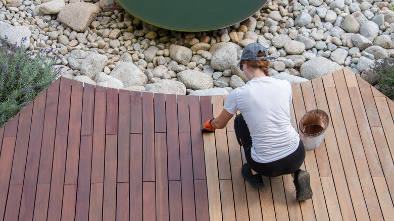 Top view of a woman staining a wooden deck outdoors