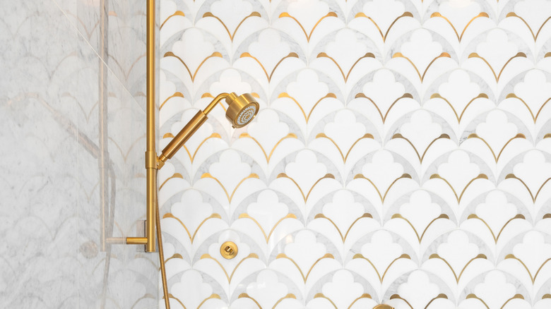 a patterned tile shower wall with gold accents and gold hardware