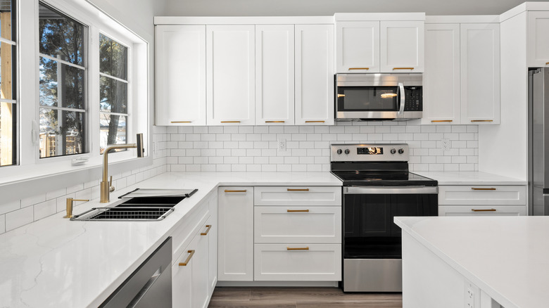 Modern kitchen with white cabinets, white counters, white subway backsplash, and gray tone LVP floors