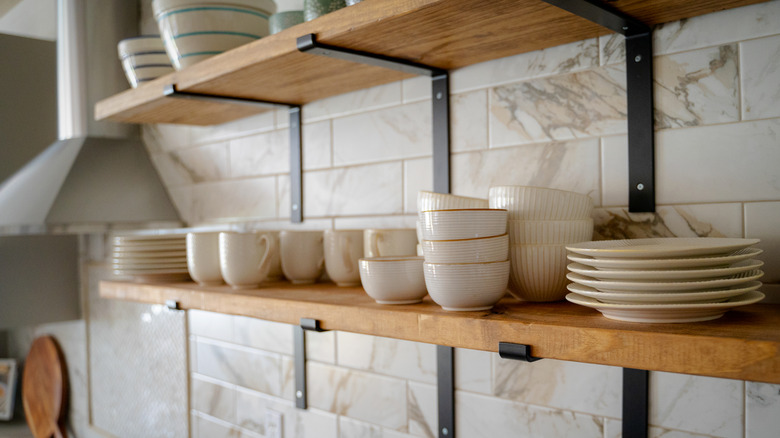 Open shelving filled with dishes mounted on a tile kitchen wall