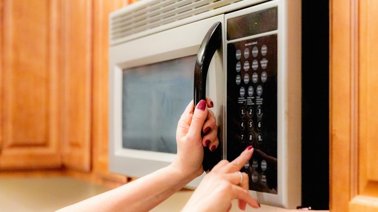 Person pushing buttons on over-the-range microwave