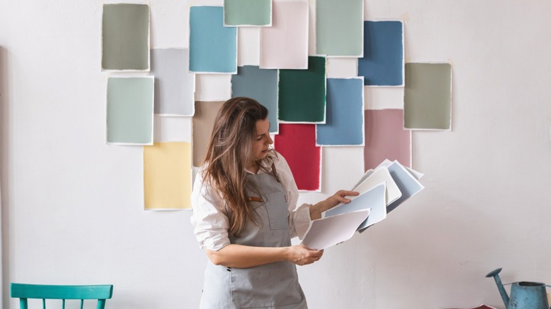 Woman holding paint samples with multiple swatches taped to an interior wall