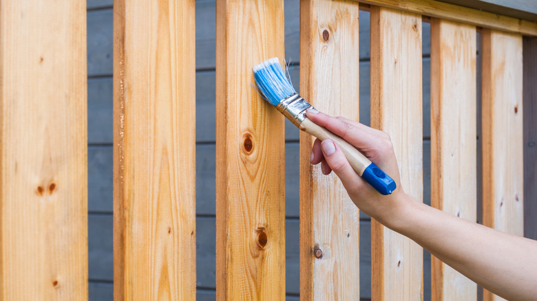 A hand staining a wood fence