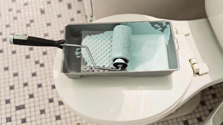 A paint roller with blue paint on a toilet