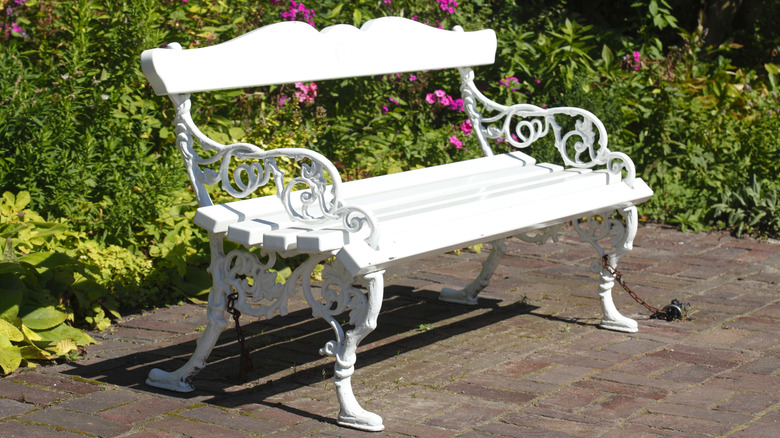 A vintage white bench on a patio in front of flowers