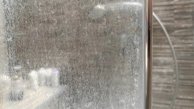 dirty glass shower wall with a shower in the background