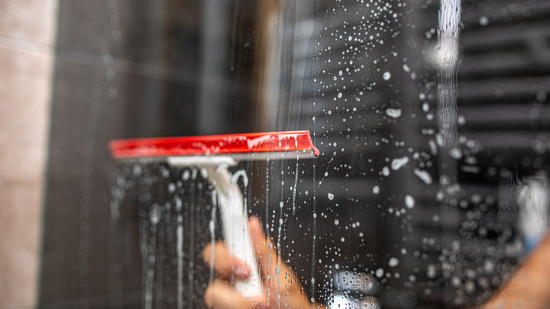 person using squeegee with red rubber to clean glass shower door