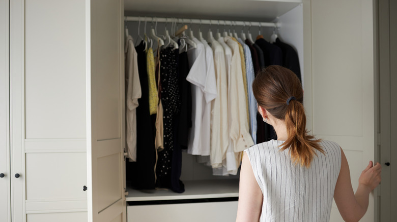 Woman wearing a white sleeveless top looking at closet full of clothes