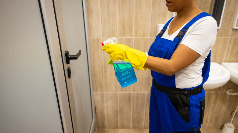 a woman sprays disinfectant on a bathroom door handle