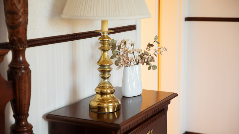 Ornate brass lamp on traditional wood nightstand beside bed