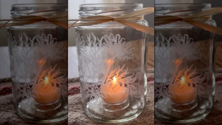 An etched glass jar with a candle inside