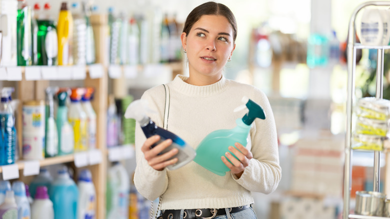 Woman holding spray bottles, trying to decide between two cleaning products in store.
