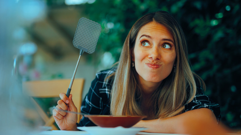 An annoyed woman holds a fly swatter as she sits by patio