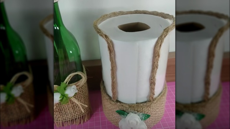 Toilet paper holder made from a clear plastic bottle with twine and flower accents
