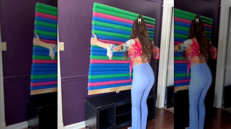 woman holding up a plywood banquette back panel covered with horizontal foam pool noodles