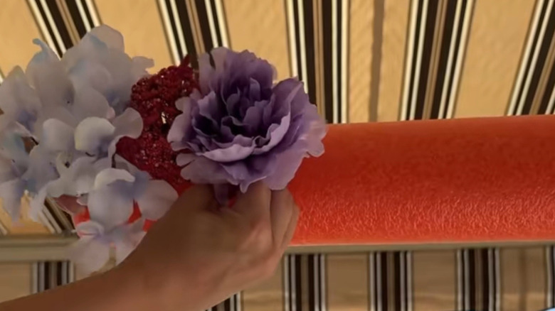 A person attaches faux flowers to a pool noodle