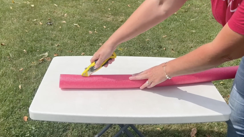 Person slicing pool noodle with box cutter