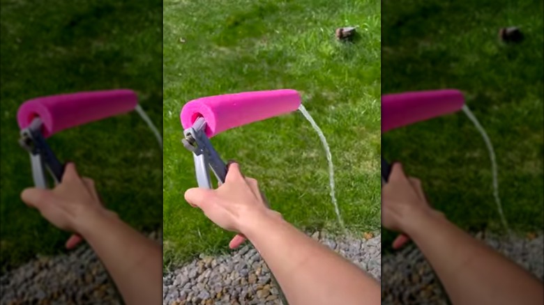 Hand holding hose nozzle with attached pool noodle extender, spraying water