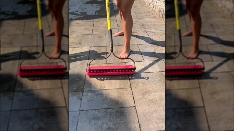 woman squeegeeing the patio using a pool noodle on a garden rake