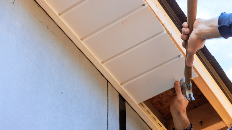 Worker installs plastic vinyl soffit at rooftop corner of rafters house