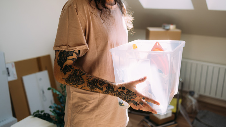 Person with tattoos holding a plastic storage box