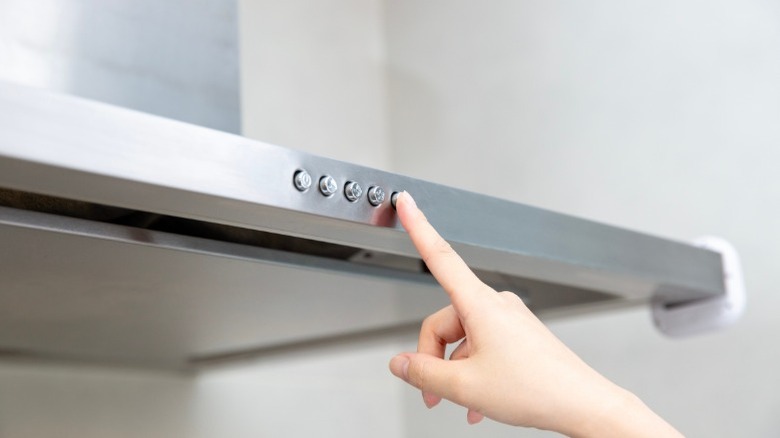 Person pressing button on a stainless steel range hood