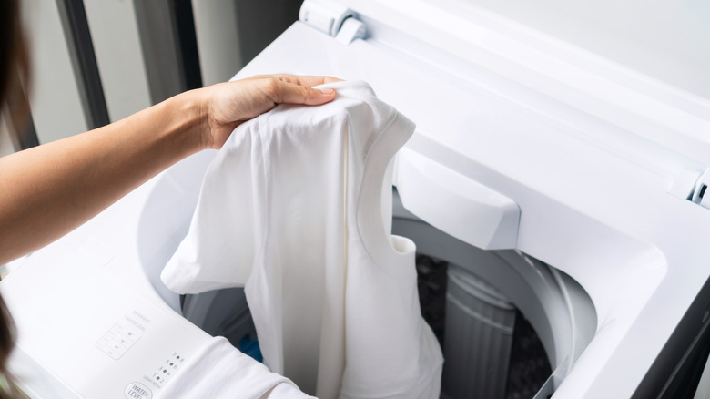 Person placing white shirt in top-loading washer