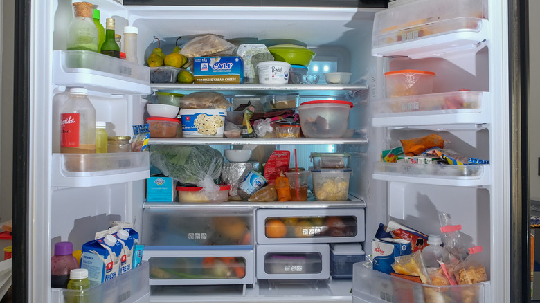 An open fridge crowded with unorganized food and drinks