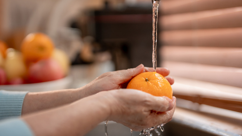 A hand washes an orange in the sink