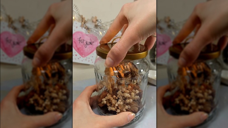 Person DIYing dried foliage tealight lantern from old glass jar