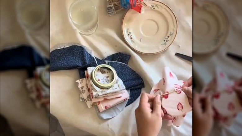 Woman fastening a strawberry-patterned fabric cloth over a glass jar over white tablecloth