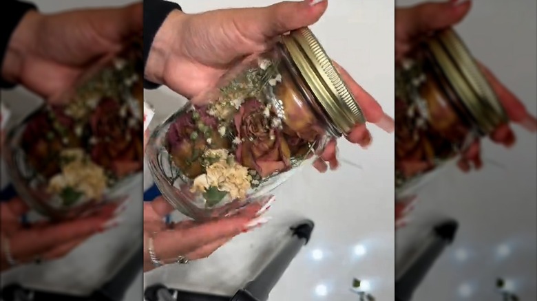 Woman showing off mason jar stuffed with nostalgic dried flowers from past bouquet over white table