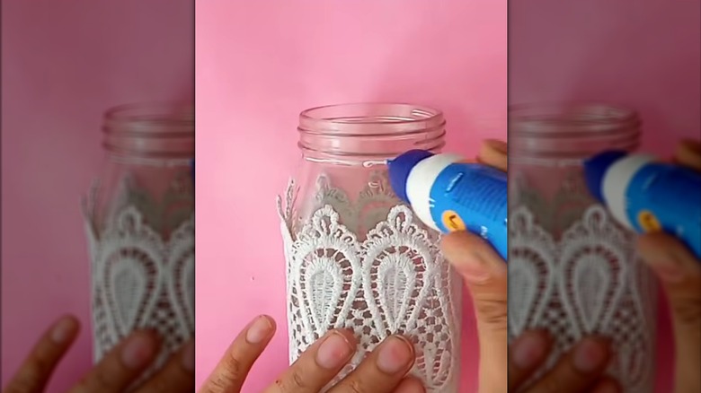 Woman wrapping glass jar with lace over pink work table